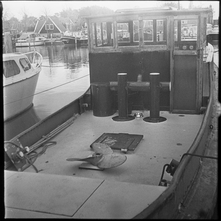 A tugboat is docked in a canal with other boats and houses in the background.