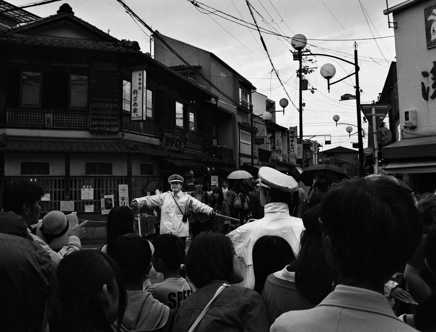 A man in a uniform with his arms outstretched directs a crowd of people on a street in Kyoto.
