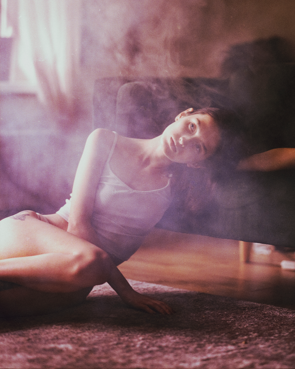 A woman in a white top is lying on a rug with her head tilted back, looking at the viewer.