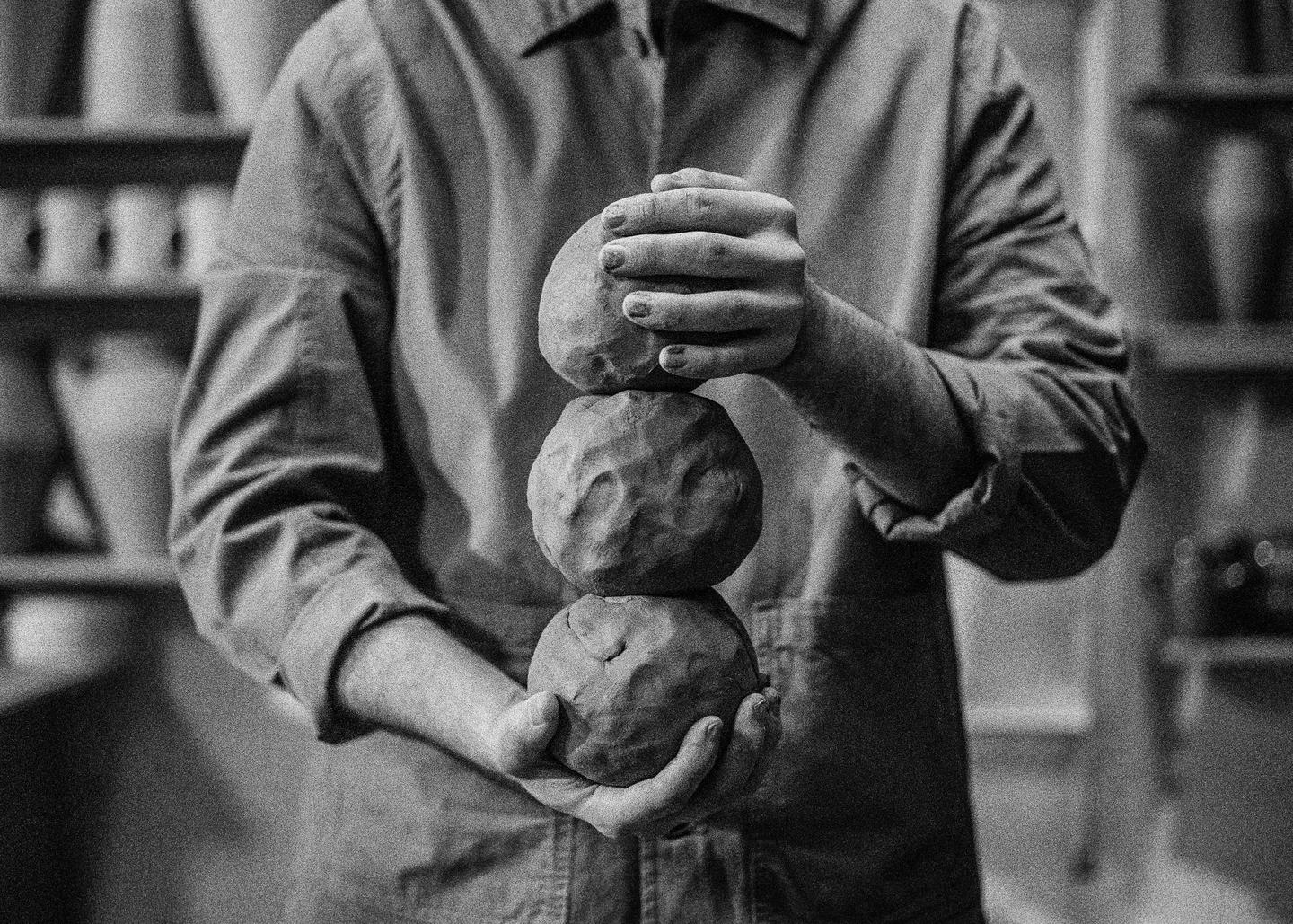 A man holds three balls of clay stacked vertically in his hands.