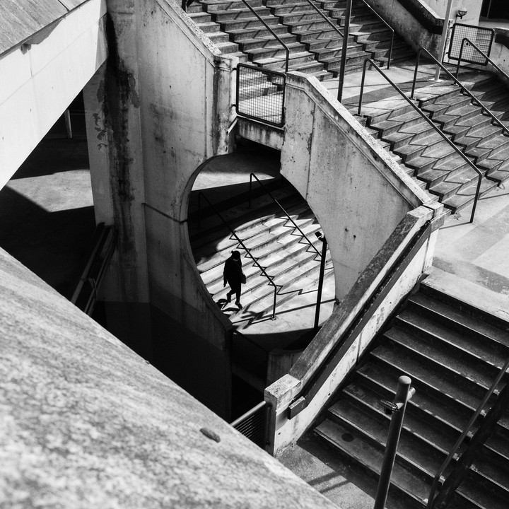 A person walks down a concrete staircase with strong shadows and railings.