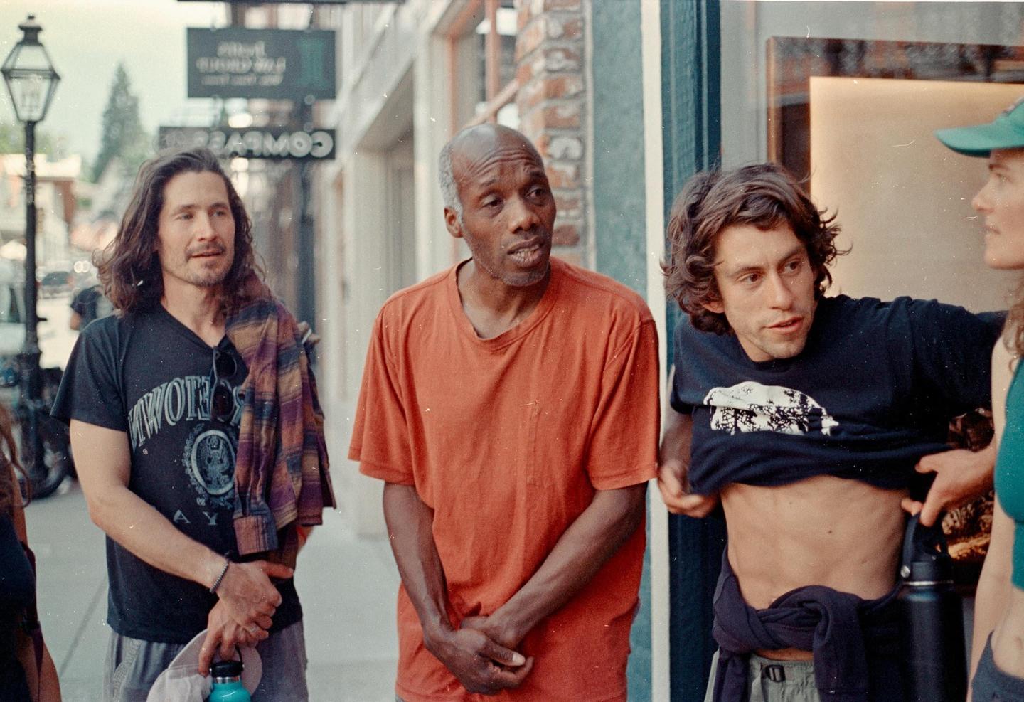 Three men and a woman are standing on a street next to a building with a sign that says "COWBOY" in reverse.