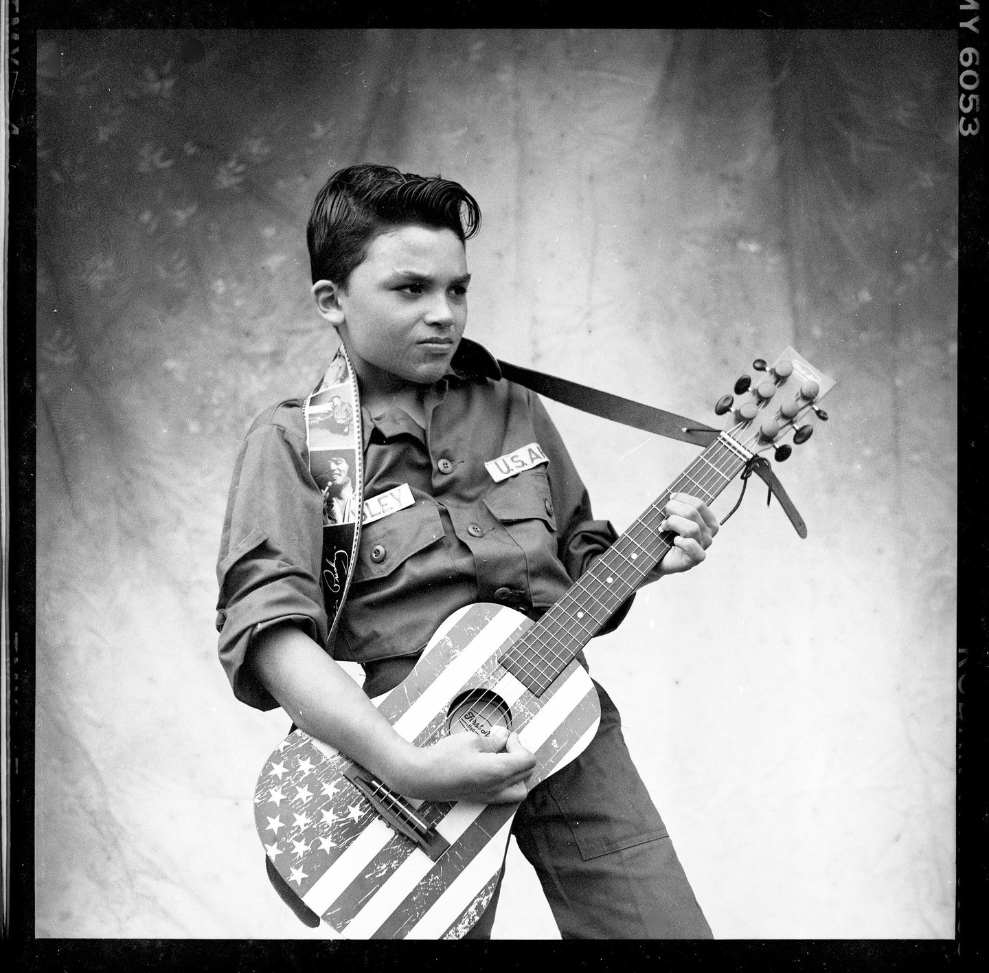 A boy in a military-style shirt plays a guitar painted with the American flag.