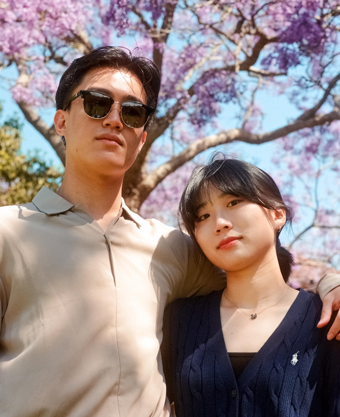 A couple stands in front of a tree with purple blossoms.