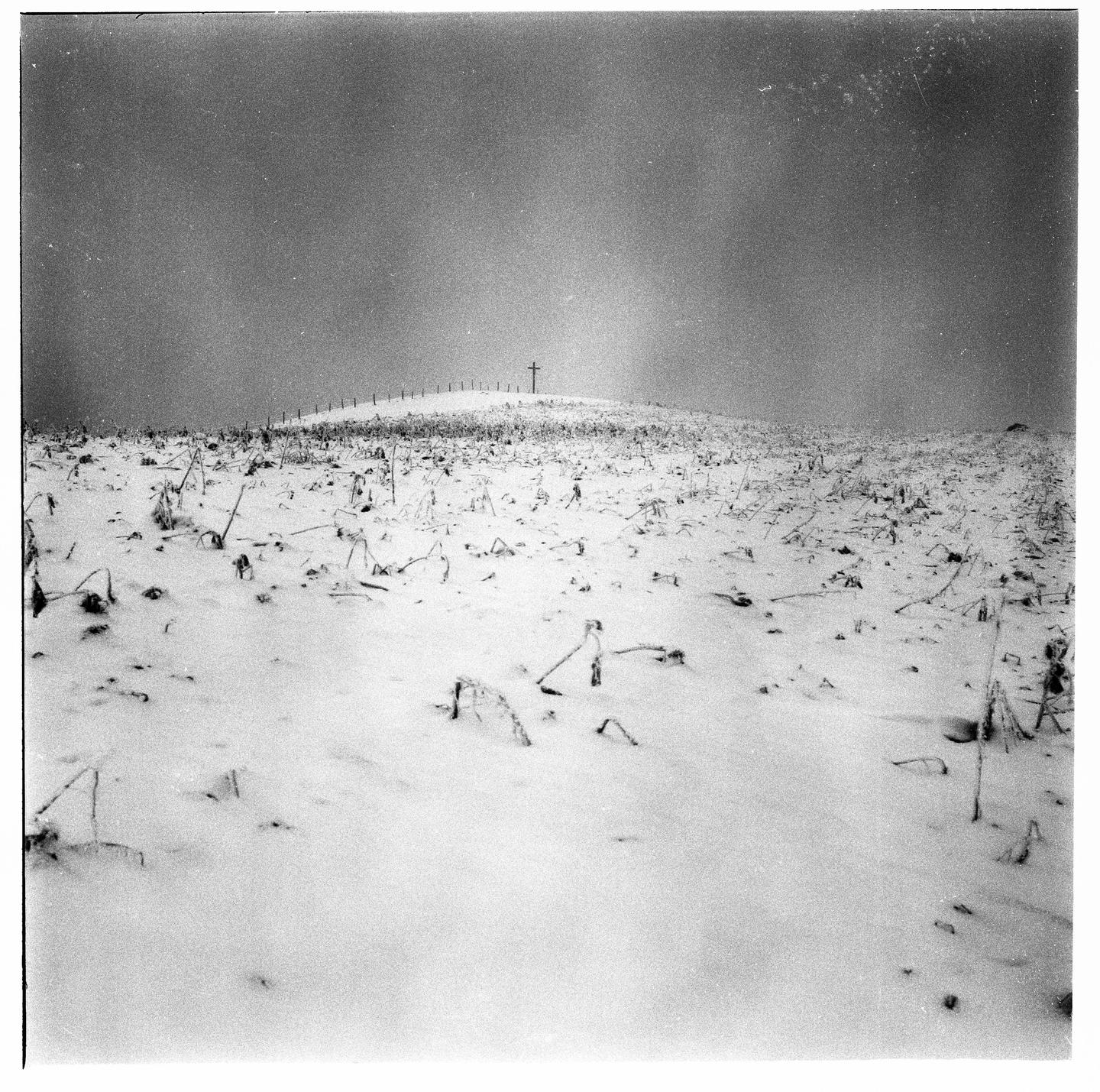 A snow-covered field with a cross on a hill under a hazy sky.