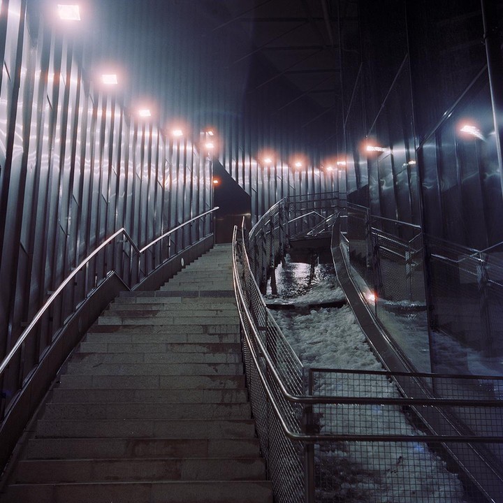 A long stairway with metal railings ascends alongside a foamy river at night.