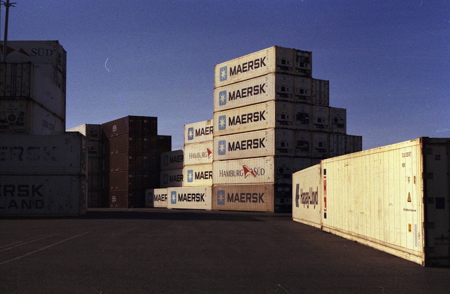 Shipping containers are stacked high in a port under a clear sky.