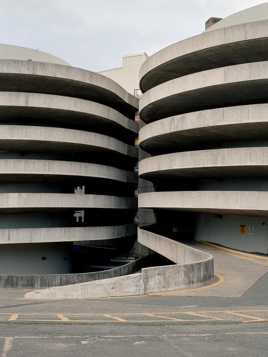 Two concrete spiral parking garages are connected by a ramp at ground level.