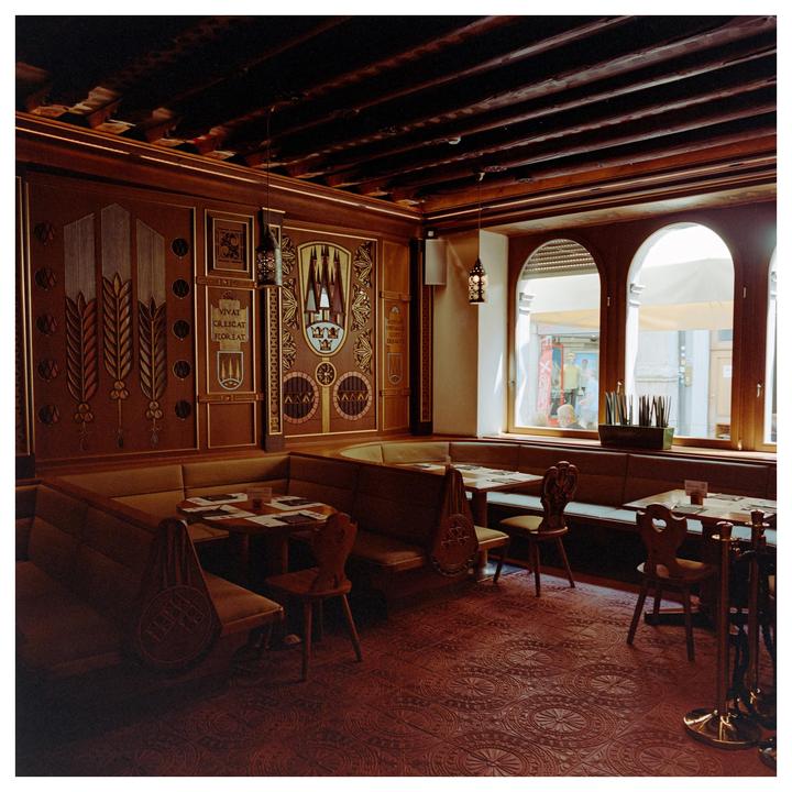 A restaurant interior features ornate wooden paneling, booth seating, and arched windows looking out onto a street.