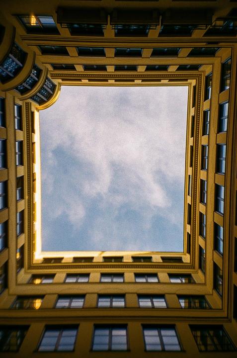 A low-angle view shows the square courtyard of a building with a blue sky and clouds visible above.