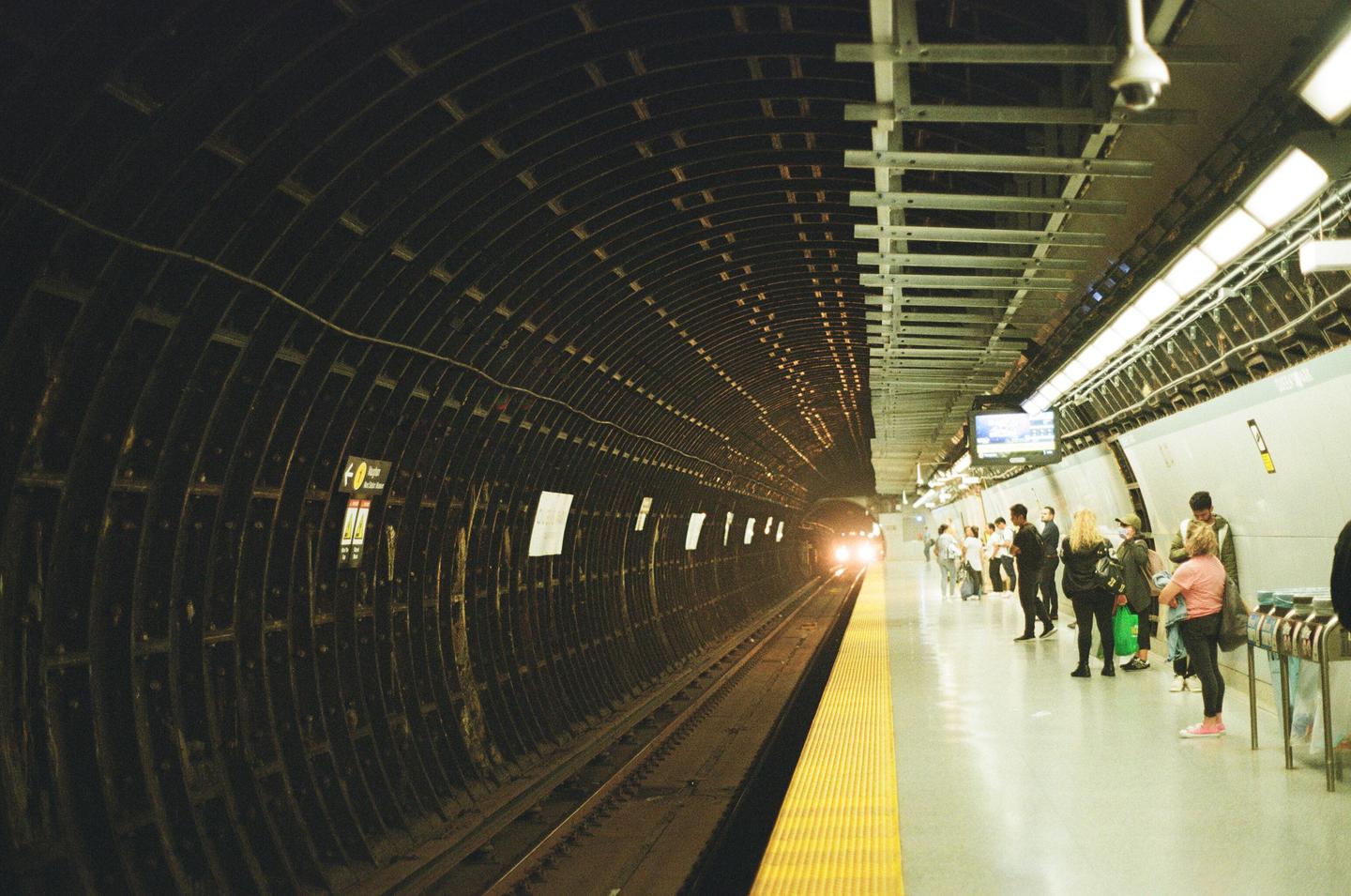 A subway train approaches a station platform where people are waiting.