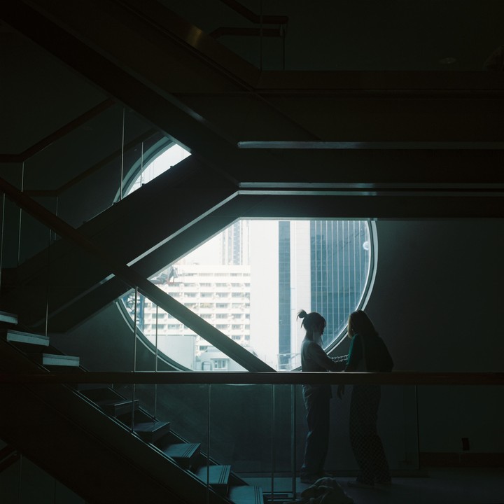 Two women stand silhouetted against a large circular window overlooking a city.