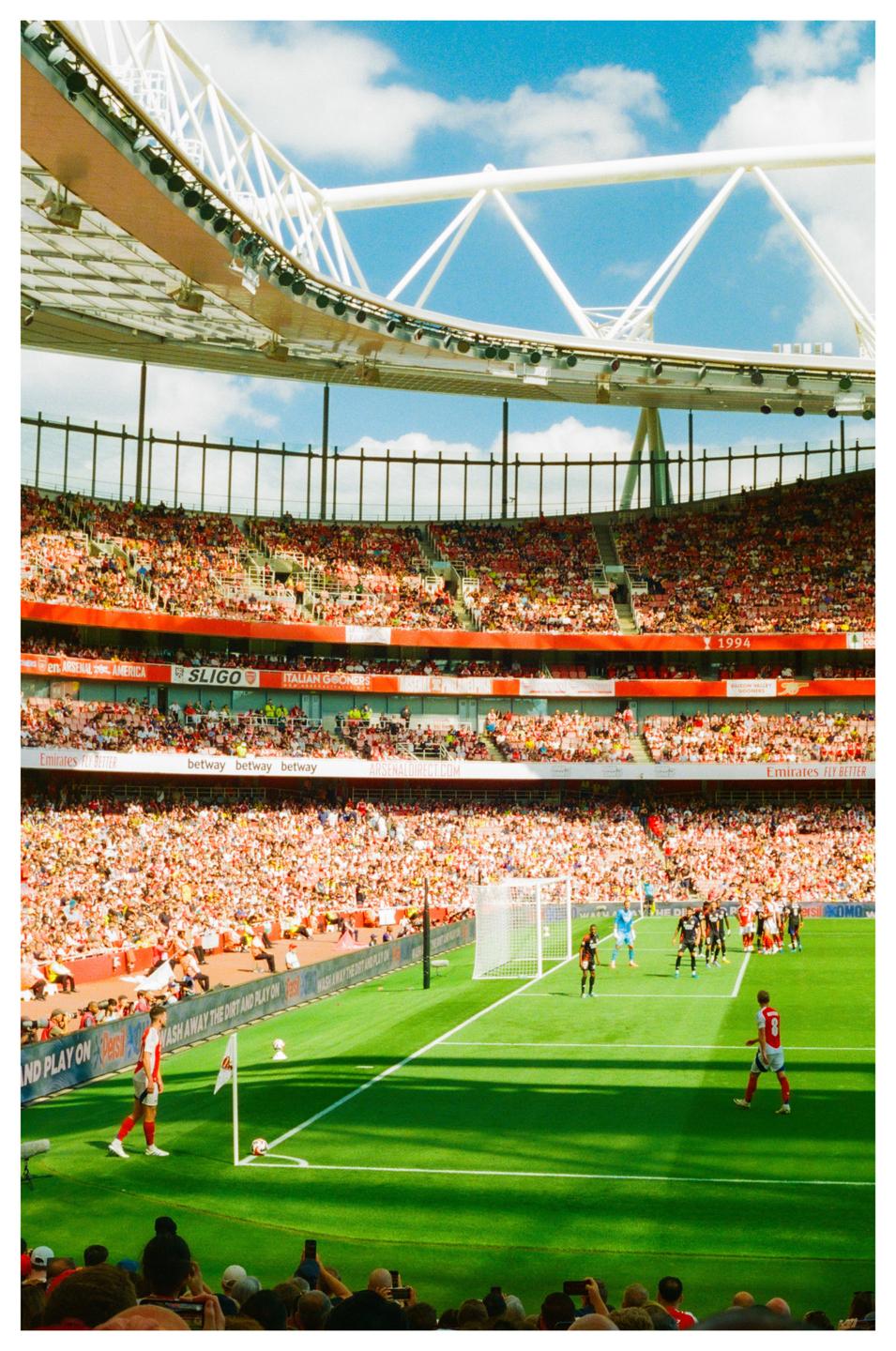 A soccer player prepares to take a corner kick in a stadium filled with spectators under a bright sky.