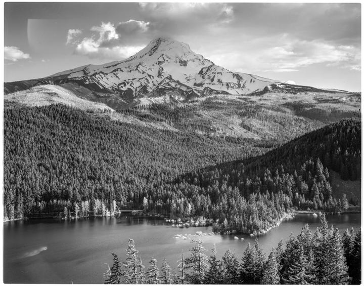 A snow-capped mountain rises above a forest and a lake.
