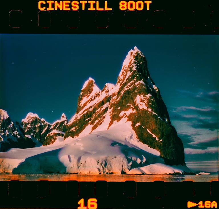 A snow-covered mountain rises from the water under a clear sky.