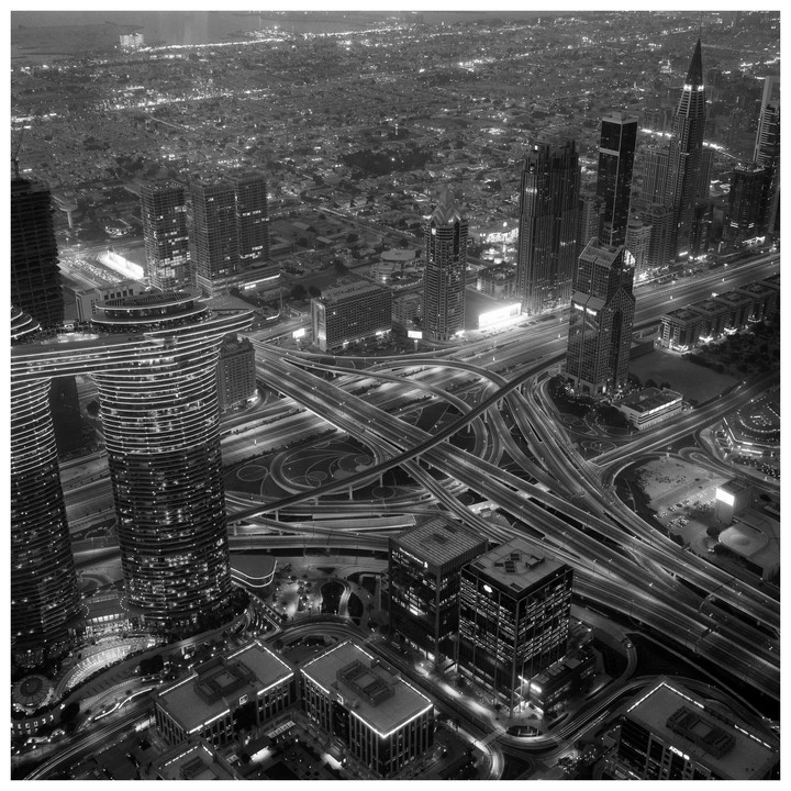 An aerial view shows a sprawling metropolis at night with numerous illuminated skyscrapers and complex highway interchanges.