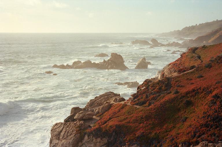 A rocky coastline with red foliage is visible next to a vast ocean with waves crashing against the shore.