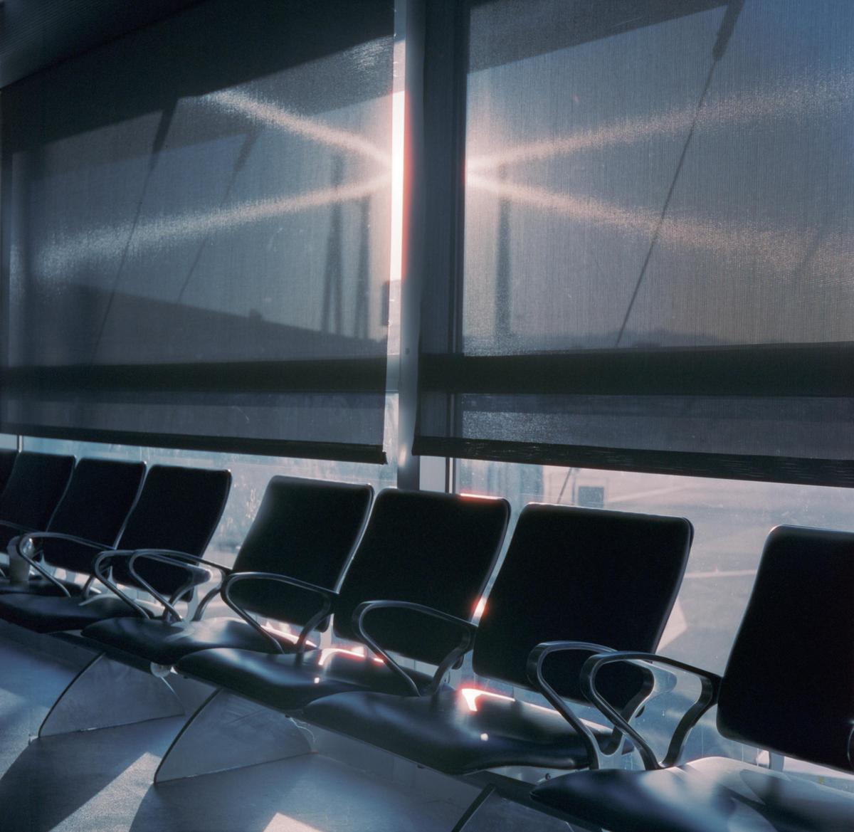 Sunlight streams through a window with blinds into an empty airport waiting area with rows of chairs.