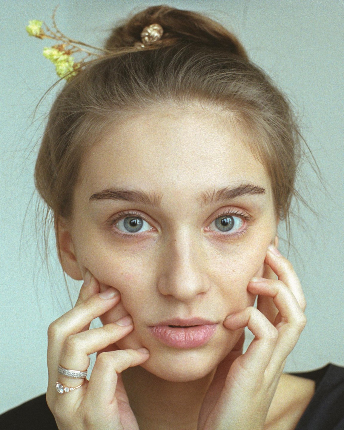 A woman with her hair in a bun holds her face with both hands.