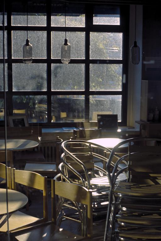 Sunlight streams through a large window into a cafe with stacked chairs and tables.