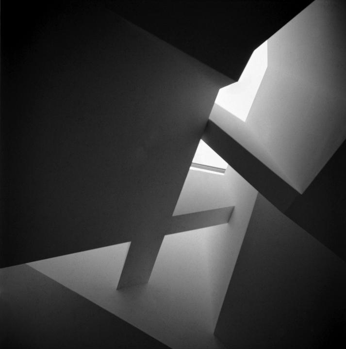 Light enters a building through geometric skylights and windows, creating abstract shapes and shadows.