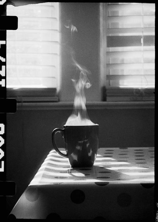 A steaming mug sits on a polka dot tablecloth next to a window with blinds.