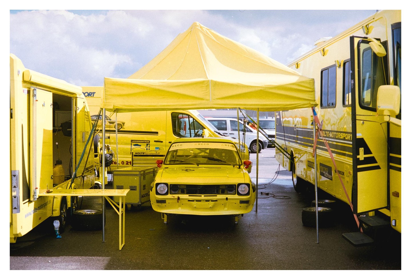 A yellow race car is parked under a yellow tent, surrounded by other yellow vehicles.