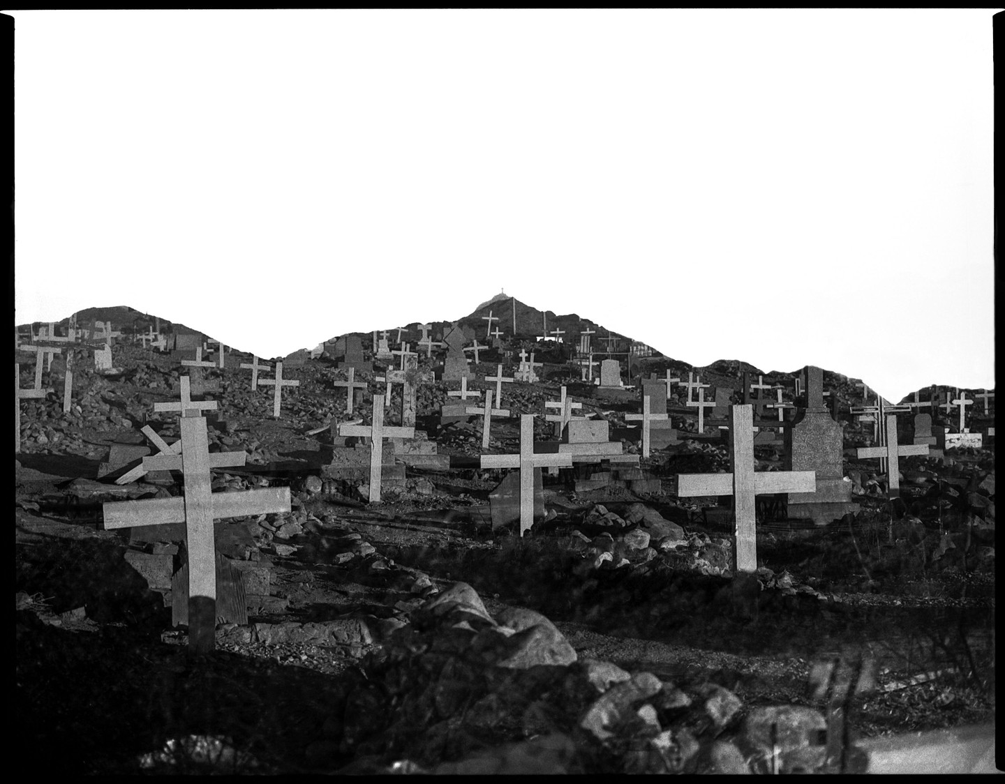 A double exposure shows a cemetery with many crosses on a hillside.