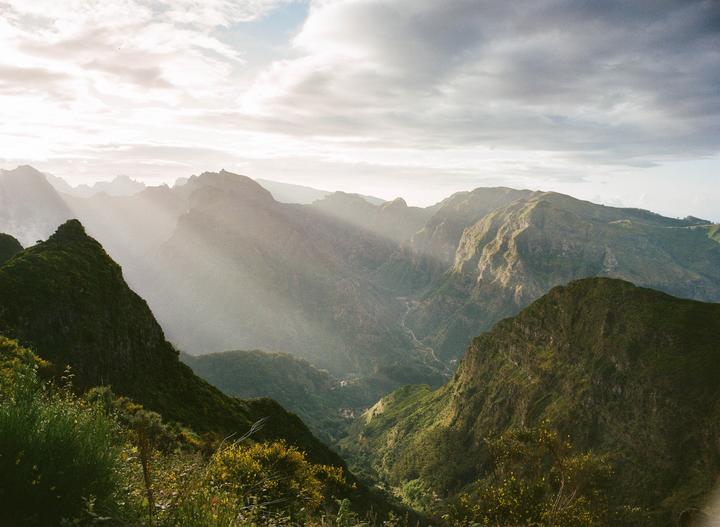 Sunlight streams through clouds over a lush green mountain valley.