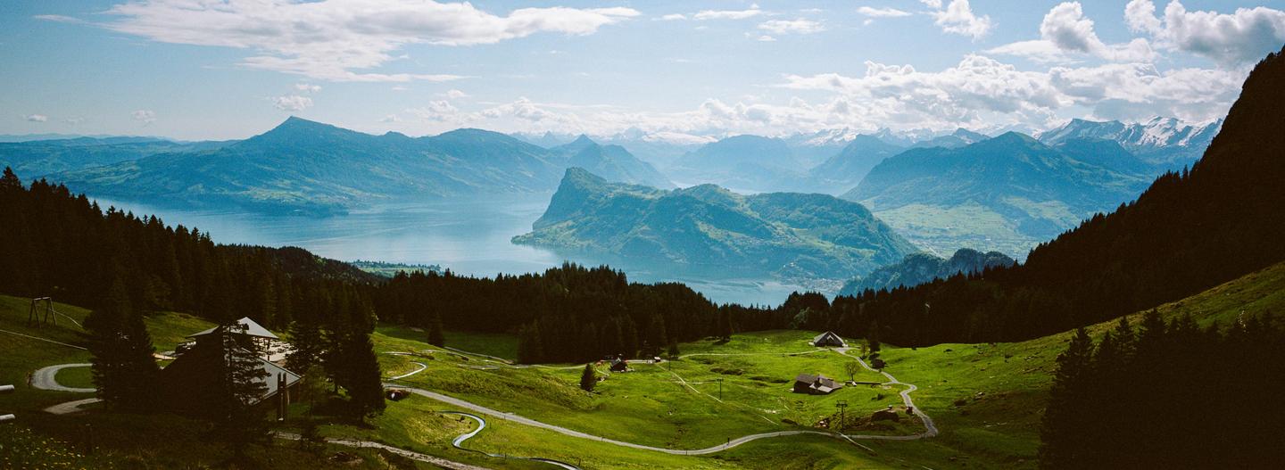 A panoramic landscape shows a lake surrounded by mountains and green hills with scattered buildings and winding paths.