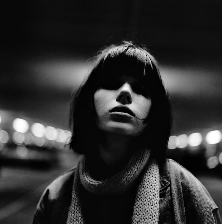 A woman with short hair and a scarf looks up at the camera in a black and white portrait.