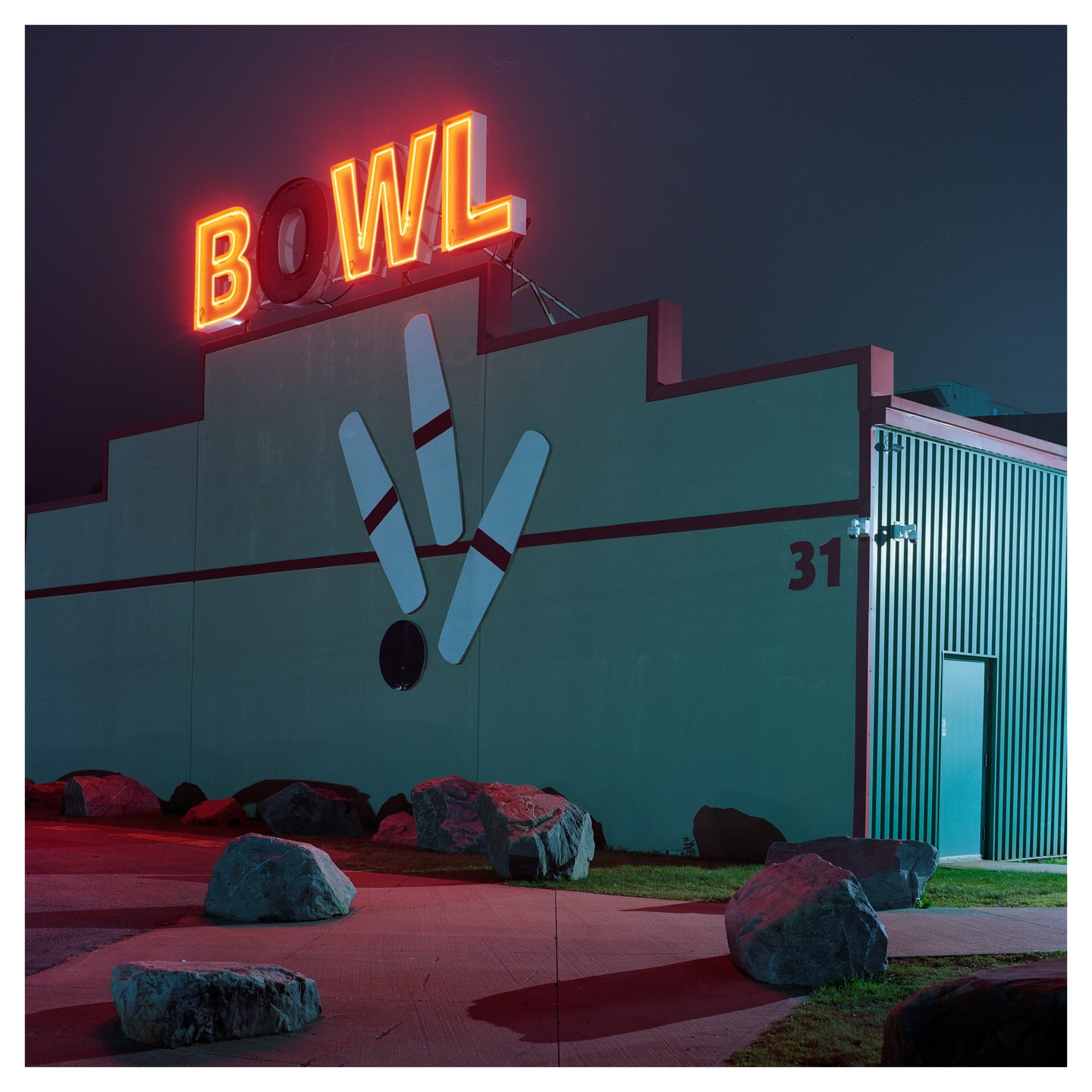 A bowling alley sign with neon letters spelling "BOWL" is illuminated at night, with bowling pins and a ball depicted below it on the building's facade.
