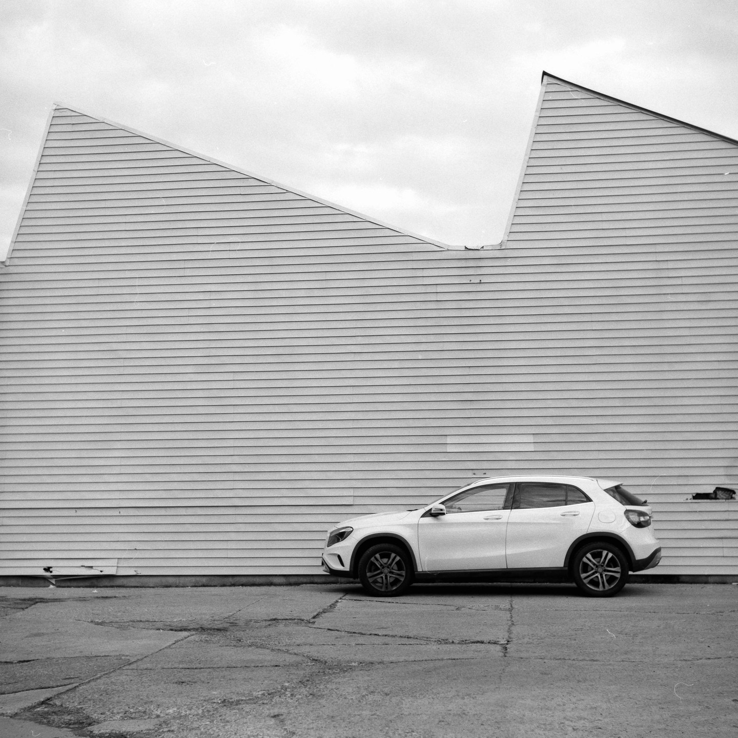 A white car is parked in front of a building with a jagged roofline.