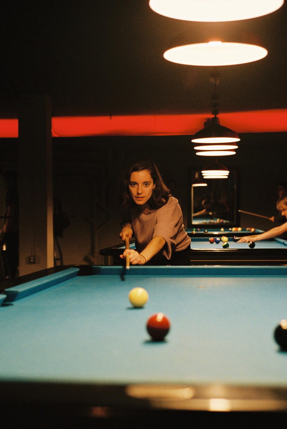 A woman leans over a pool table, holding a cue stick and aiming at a yellow ball.