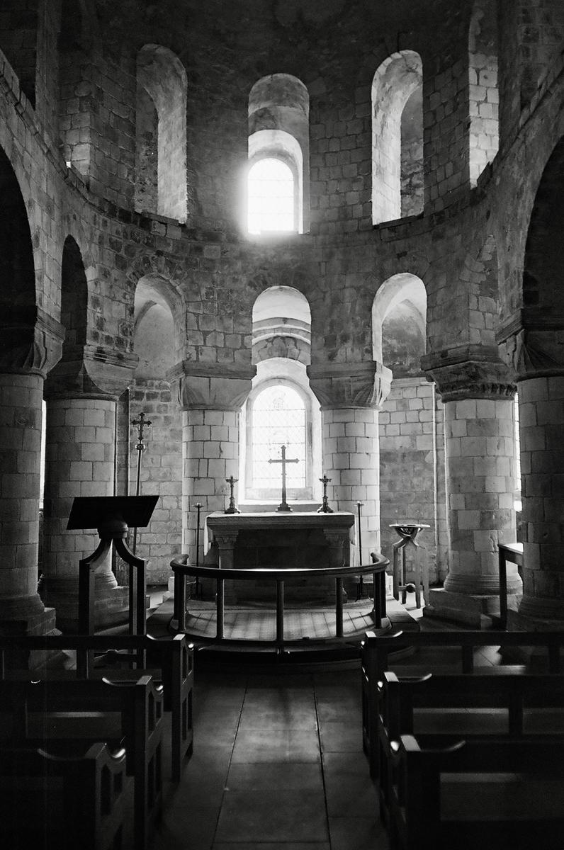 A stone church interior with an altar and cross is illuminated by light from a window.