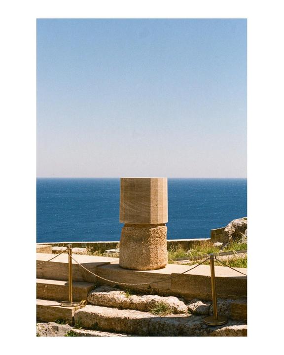 A stone column stands on a stone platform with the ocean and sky in the background.