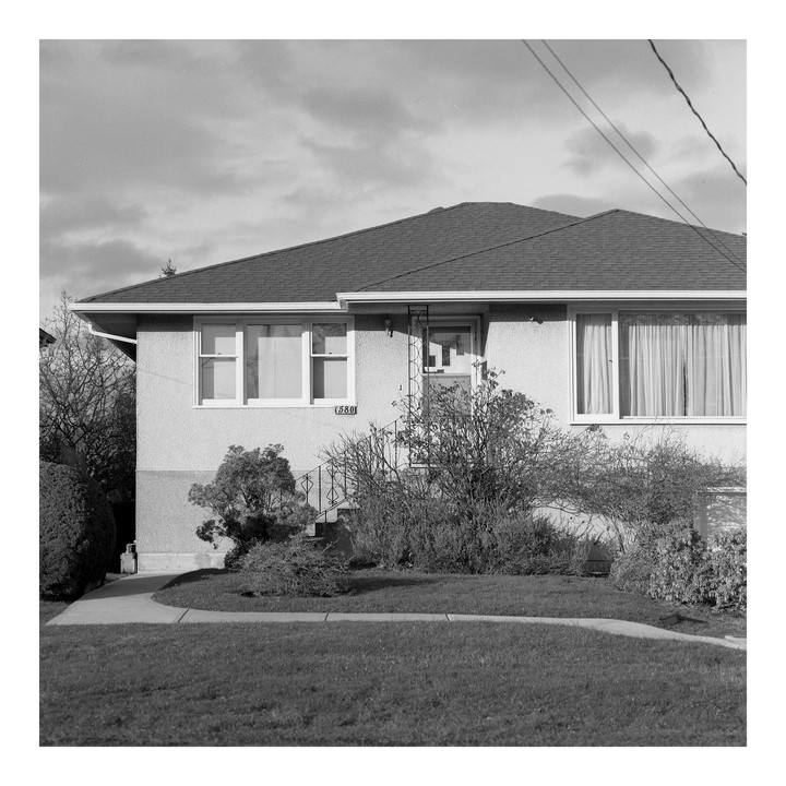 A house with a number 580 on its facade is seen from the street, with a grassy lawn and bushes in front.