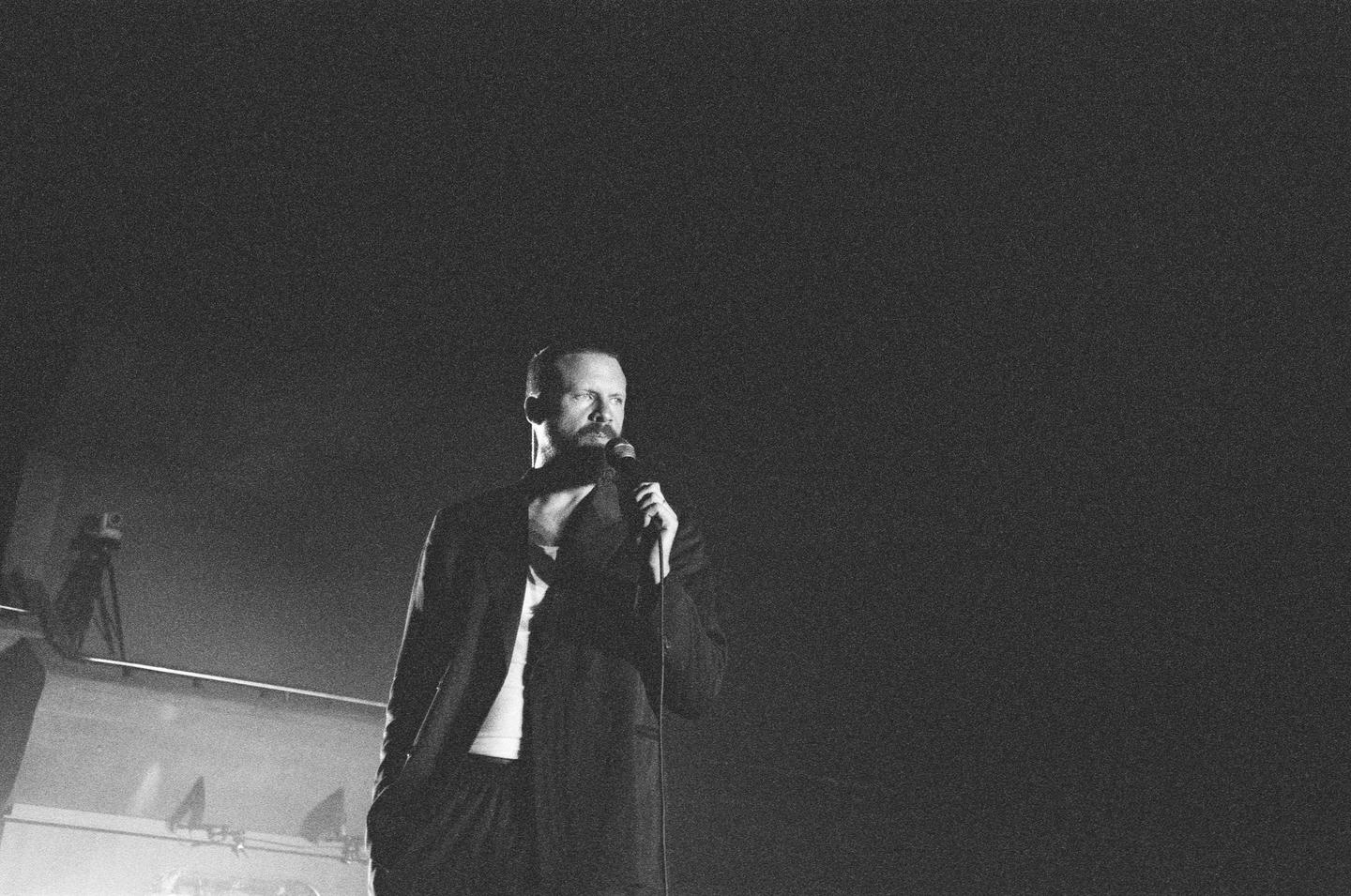 A man with a beard and mustache holds a microphone and looks to the right.