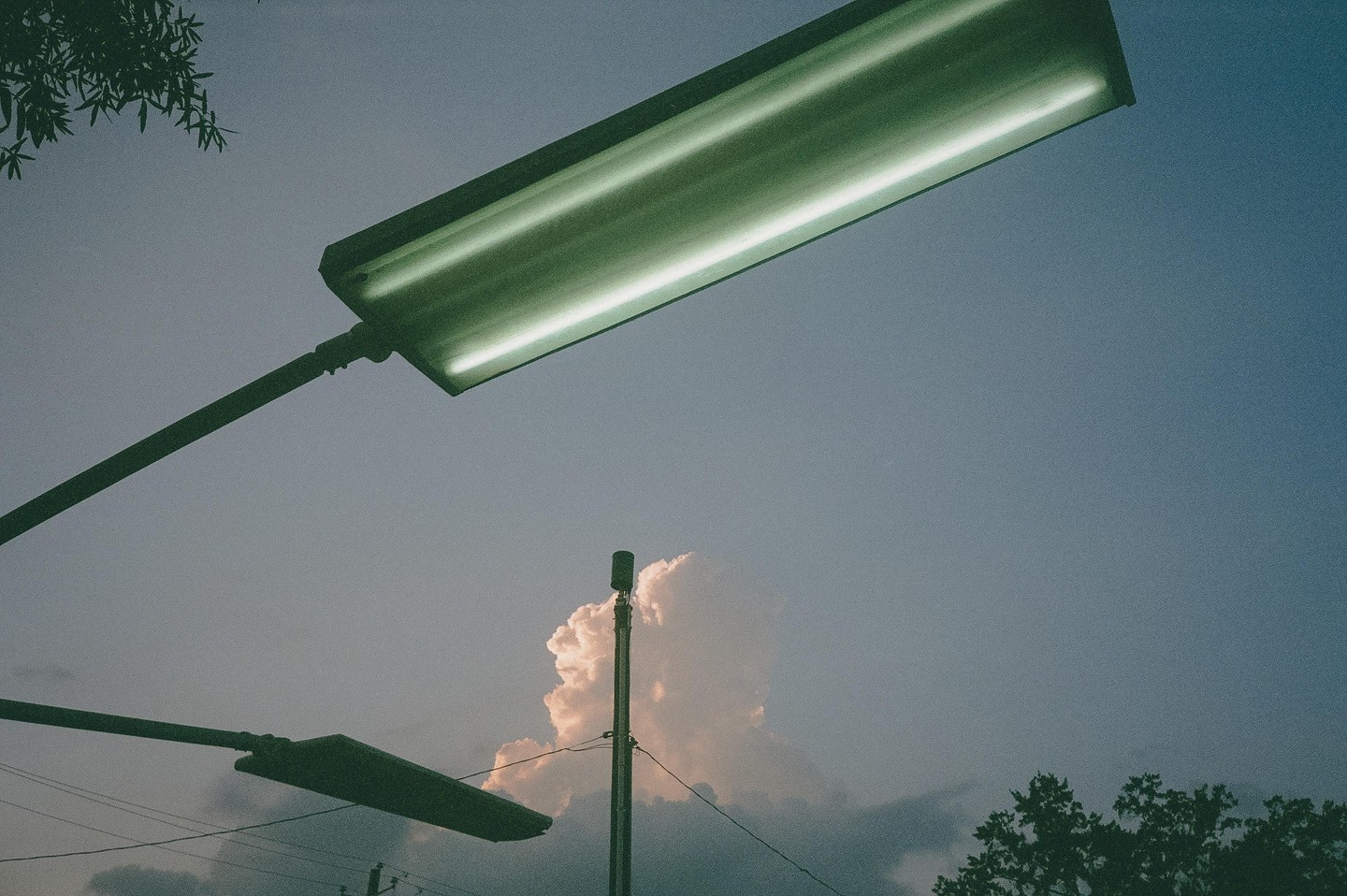 Two streetlights and a utility pole are silhouetted against a cloudy sky at dusk.