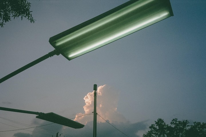 Two streetlights and a utility pole are silhouetted against a cloudy sky at dusk.