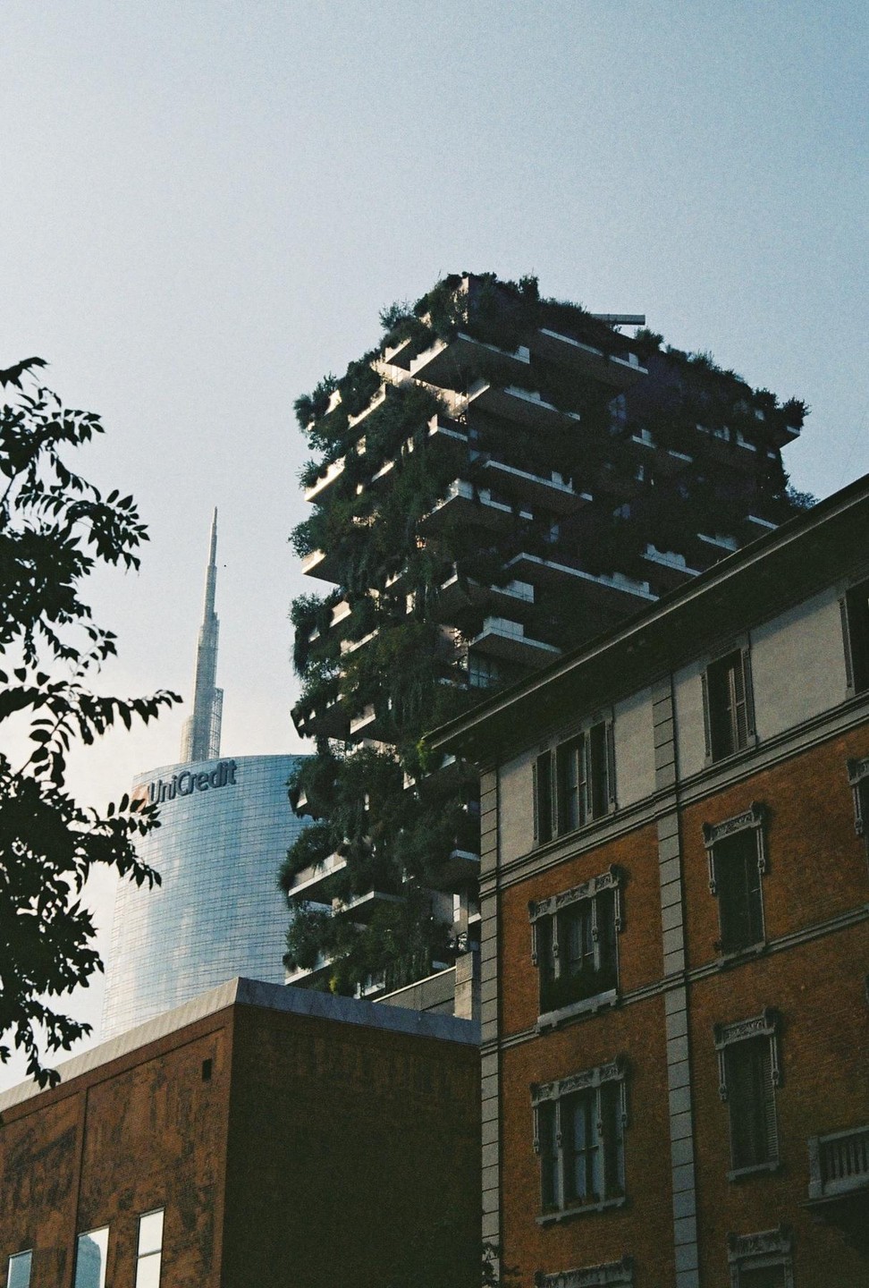 A tall building covered in plants stands next to a glass skyscraper and a brick building.