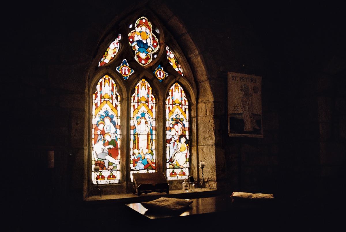 A stained glass window with religious figures is visible in a dark room.