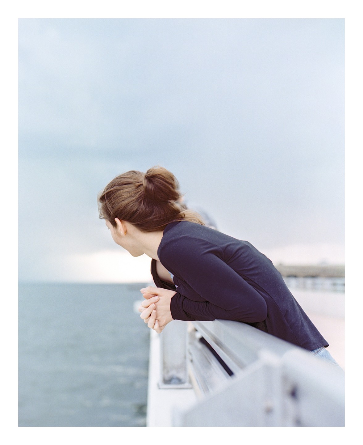 A woman leans over a railing looking down at the water.