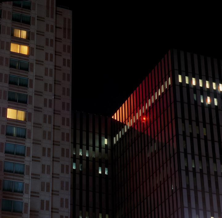 Two buildings with illuminated windows are visible at night, one with a red light reflecting on its facade.