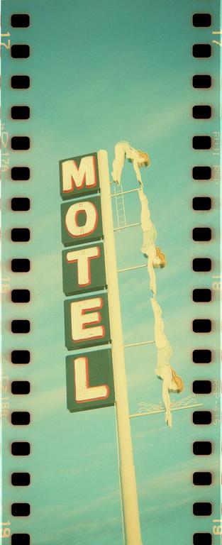 A motel sign with three diving women is set against a clear sky.