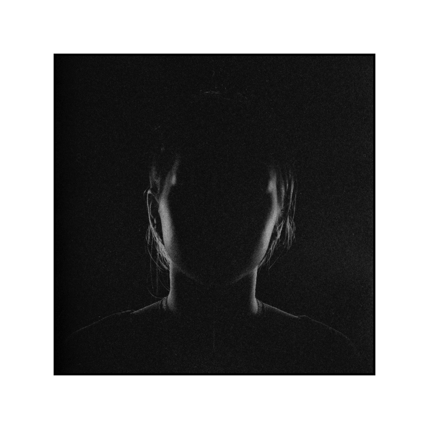 A woman is visible from the shoulders up, with her face in shadow and only the outline of her head and shoulders illuminated.