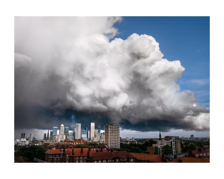 A large, dark cloud hangs over the London skyline, with blue sky visible above the cloud.
