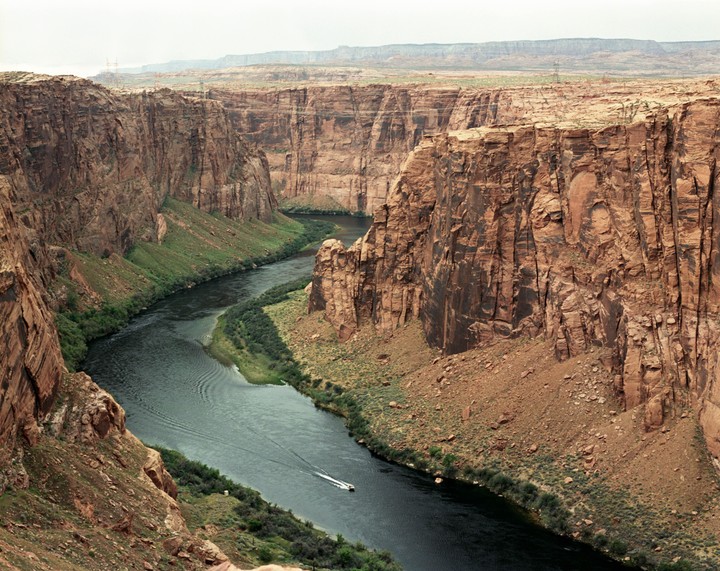 A boat travels down a winding river through a deep canyon.