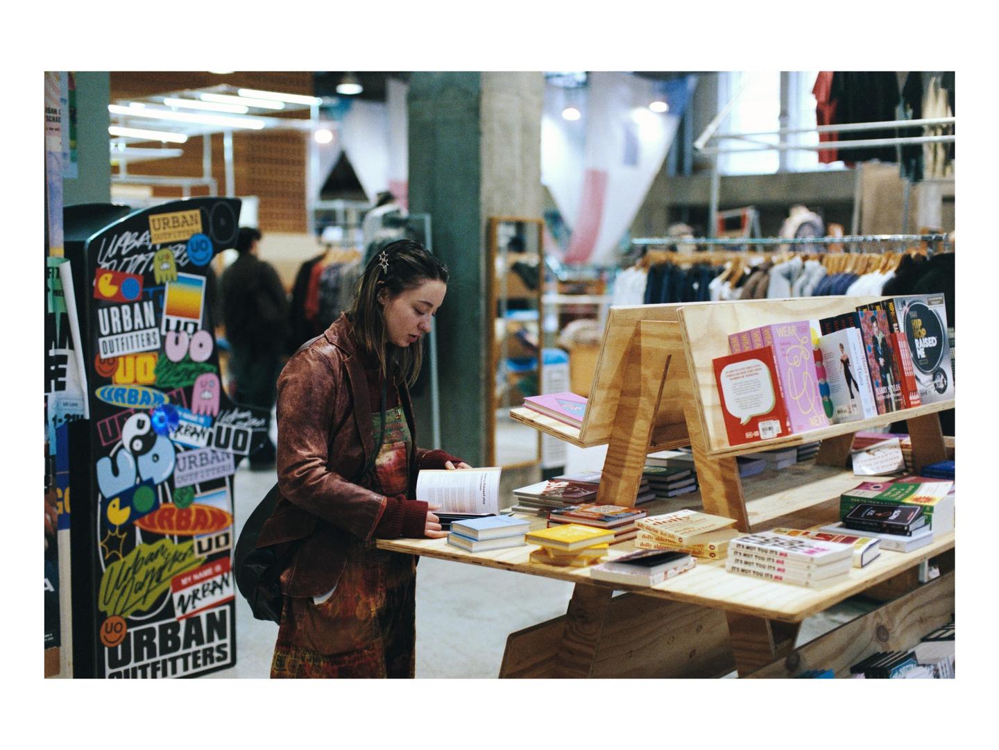 A woman in a brown jacket is looking at a book in a store.