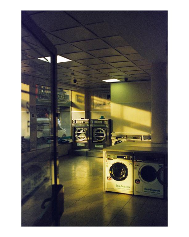 Sunlight streams into a laundromat with several washing machines and dryers.